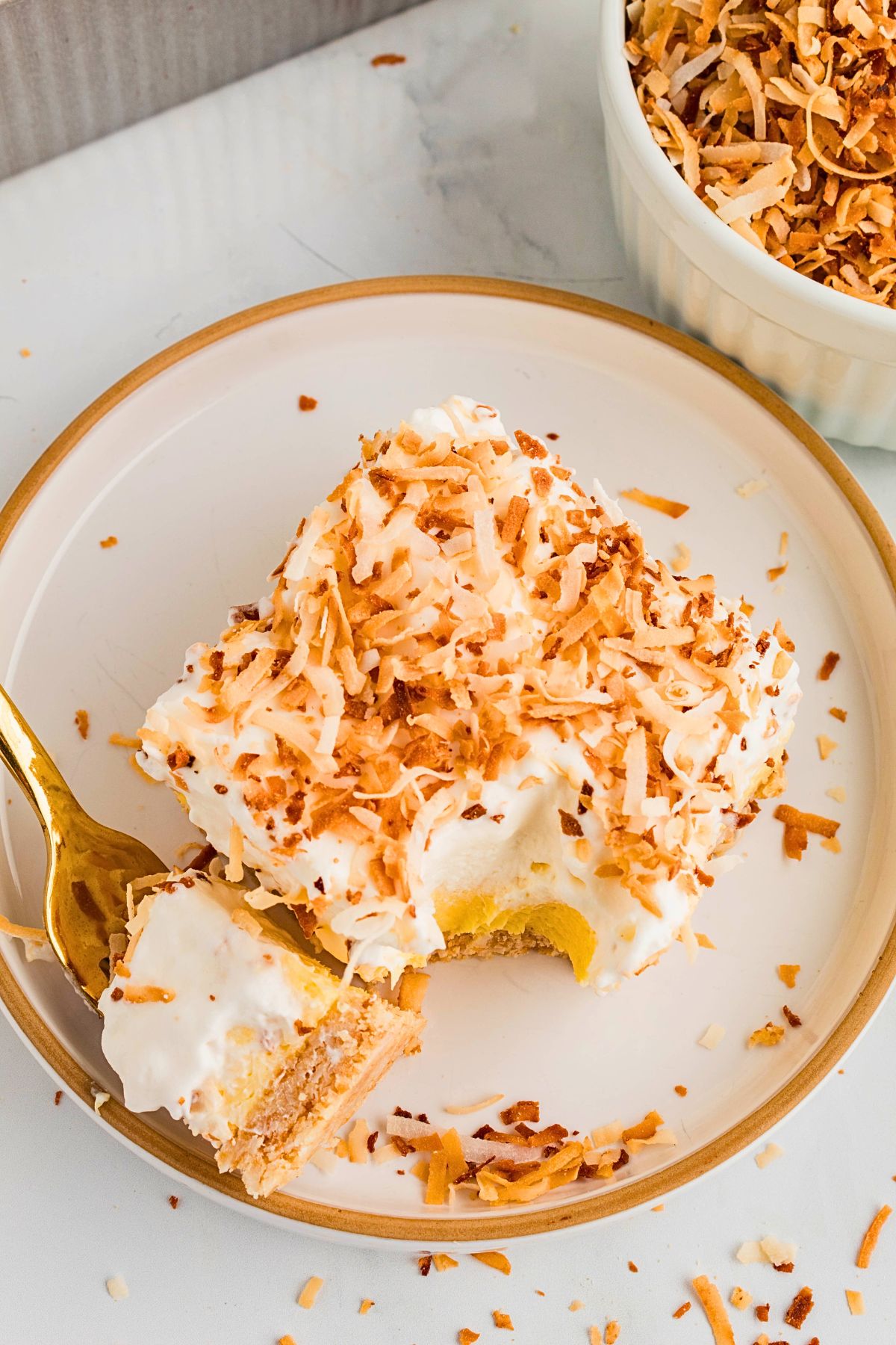 Slice of creamy pie on a white plate, topped with toasted coconut. 