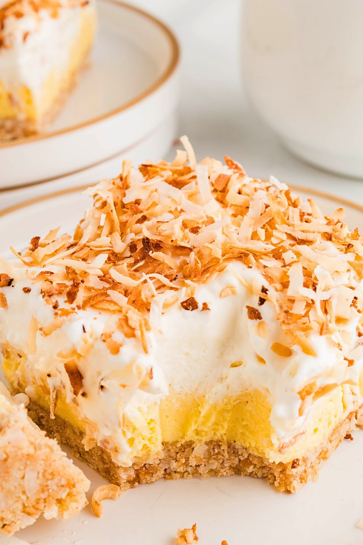 Coconut delight on a small white plate topped with whipped cream and toasted coconut flakes with a small bite missing. 