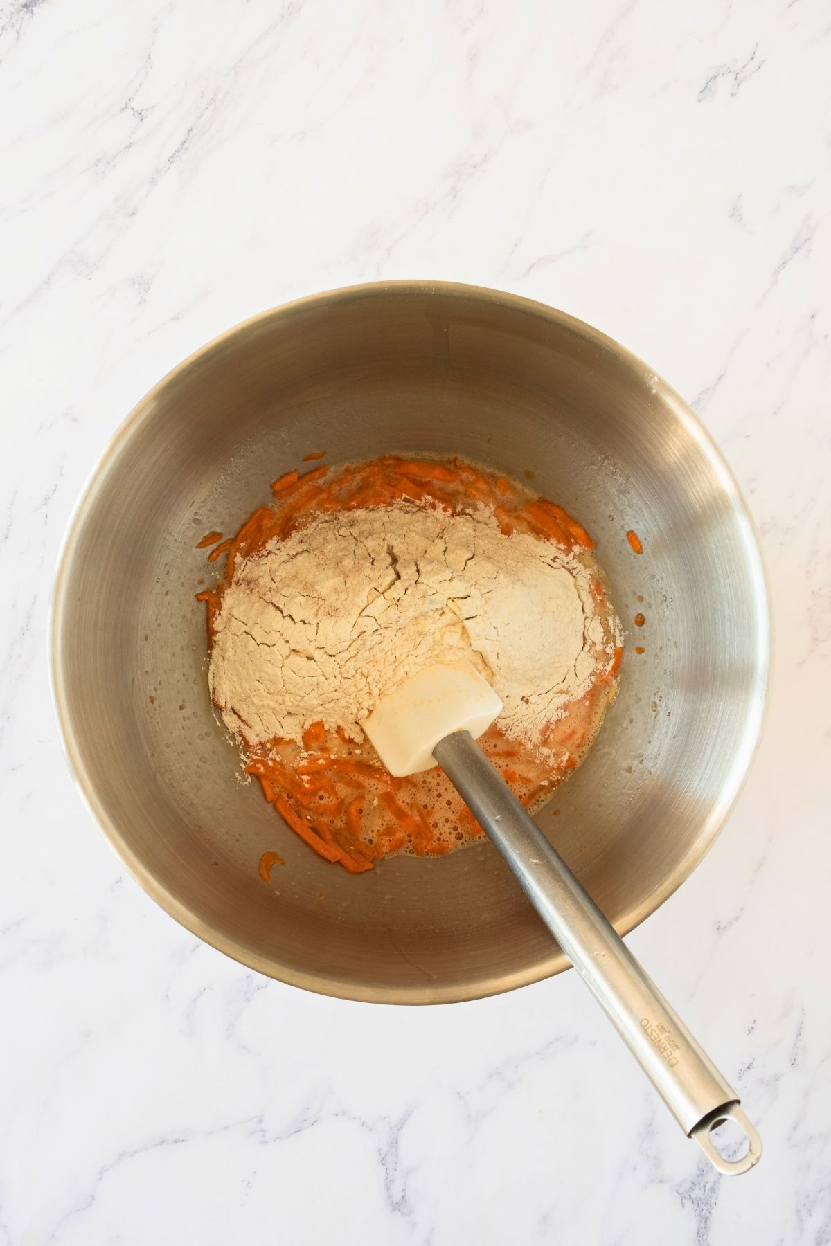 Shredded carrots mixed in a silver bowl with flour and other cake ingredients. 