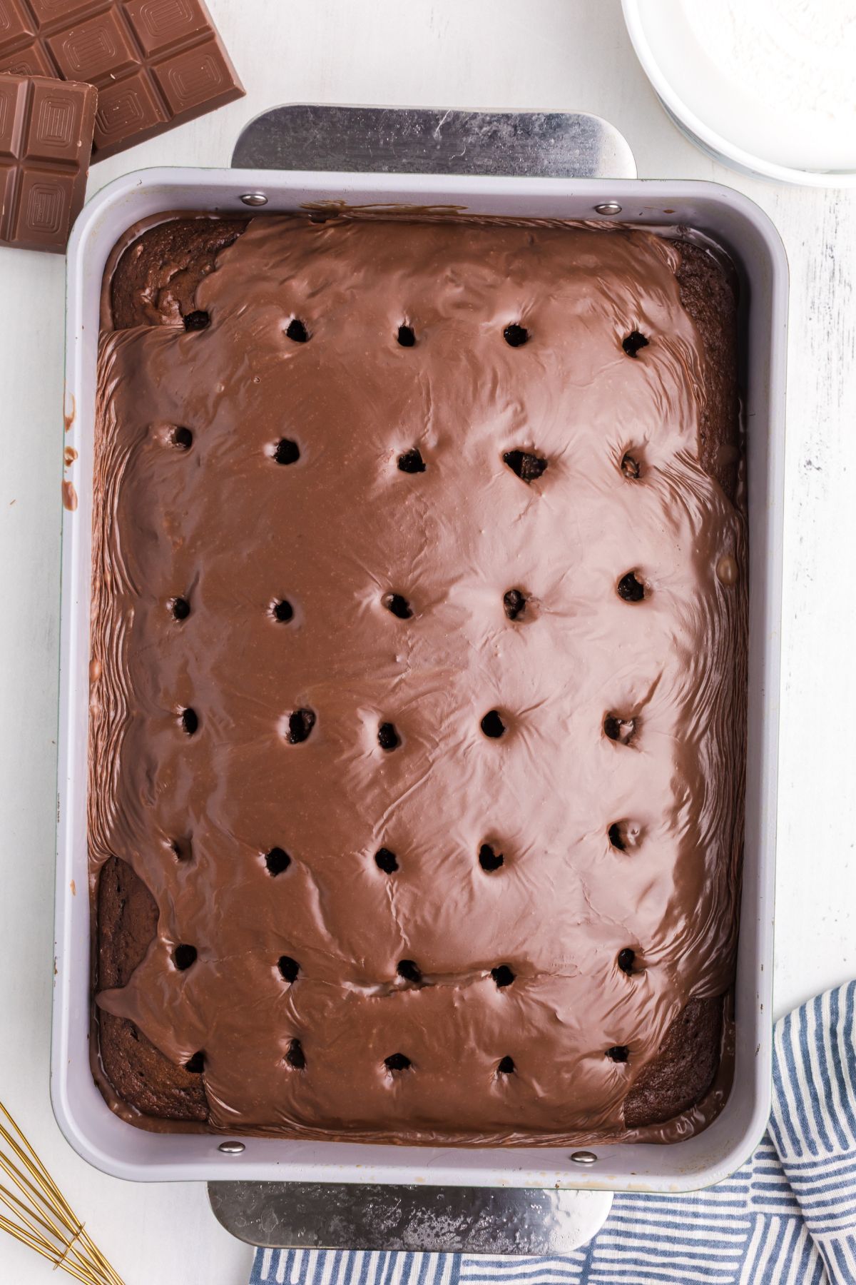 Melted chocolate and sweetened condensed milk poured into holes in a chocolate cake.