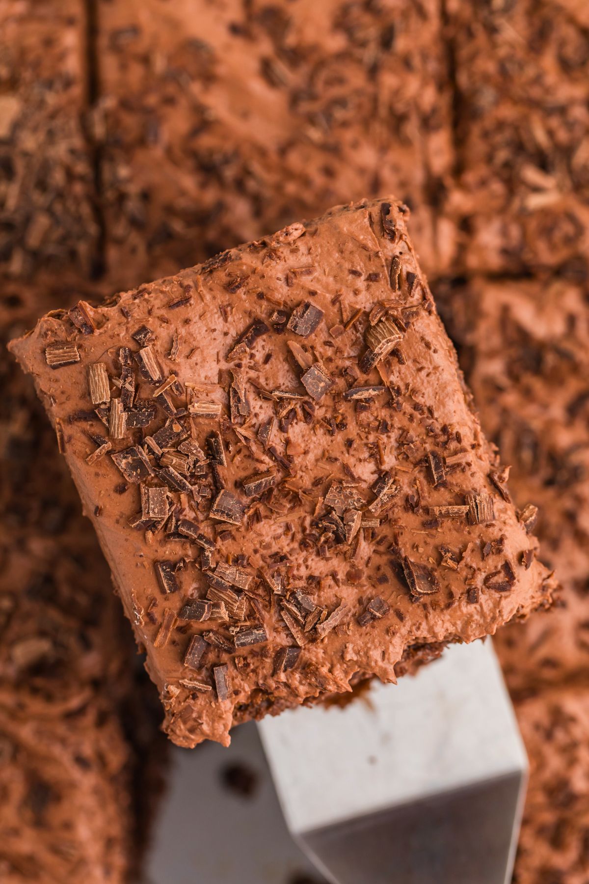 Piece of chocolate poke cake on a spatula topped with whipped cream and chocolate shavings.