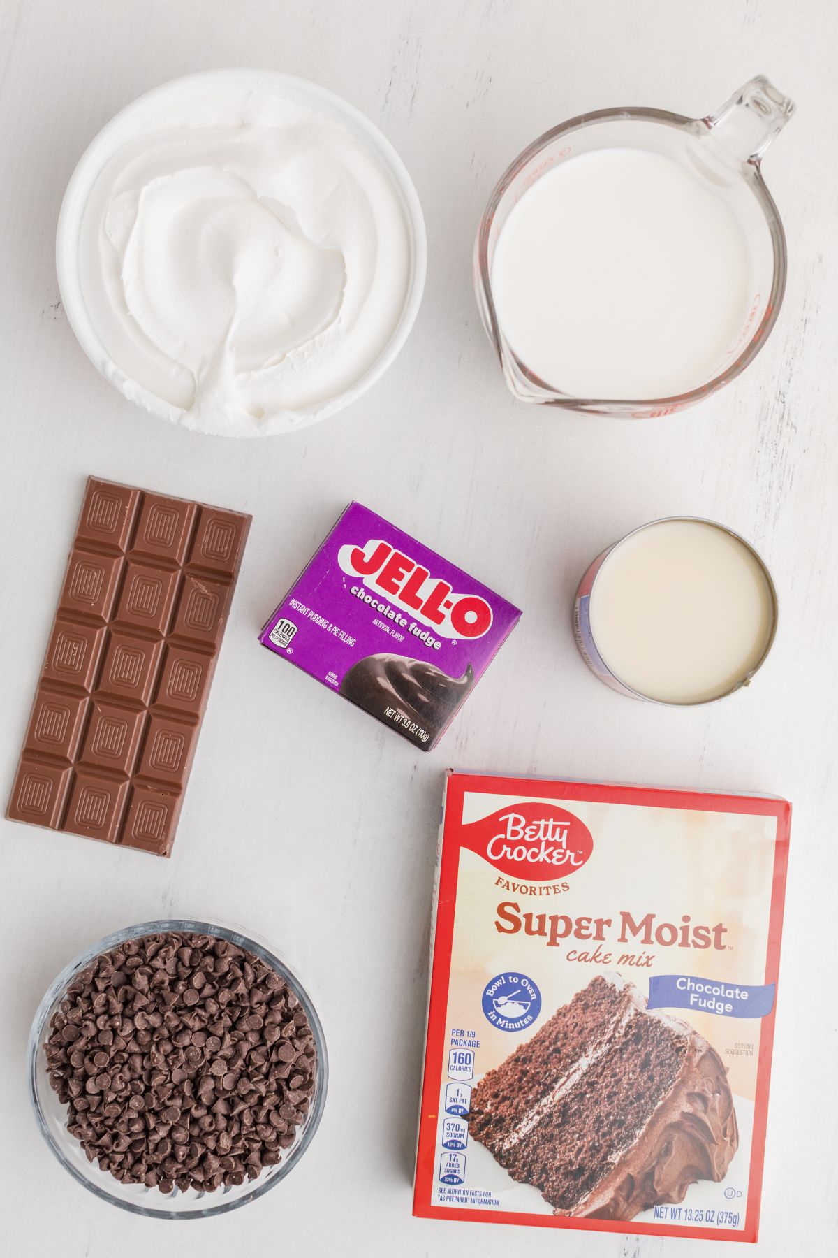 Ingredients needed to make chocolate poke cake, on a white marble table.