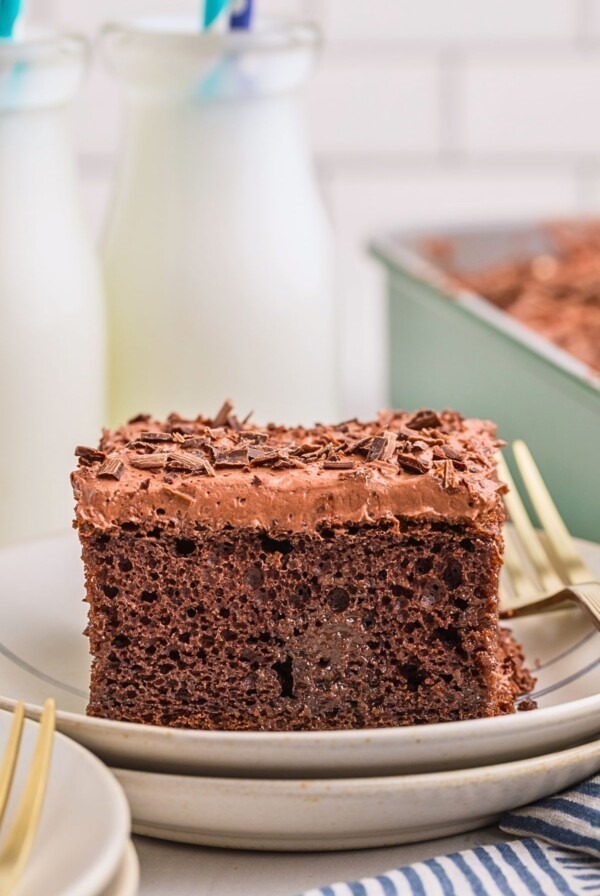 Chocolate poke cake on a plate with bottles of milk behind the plate.