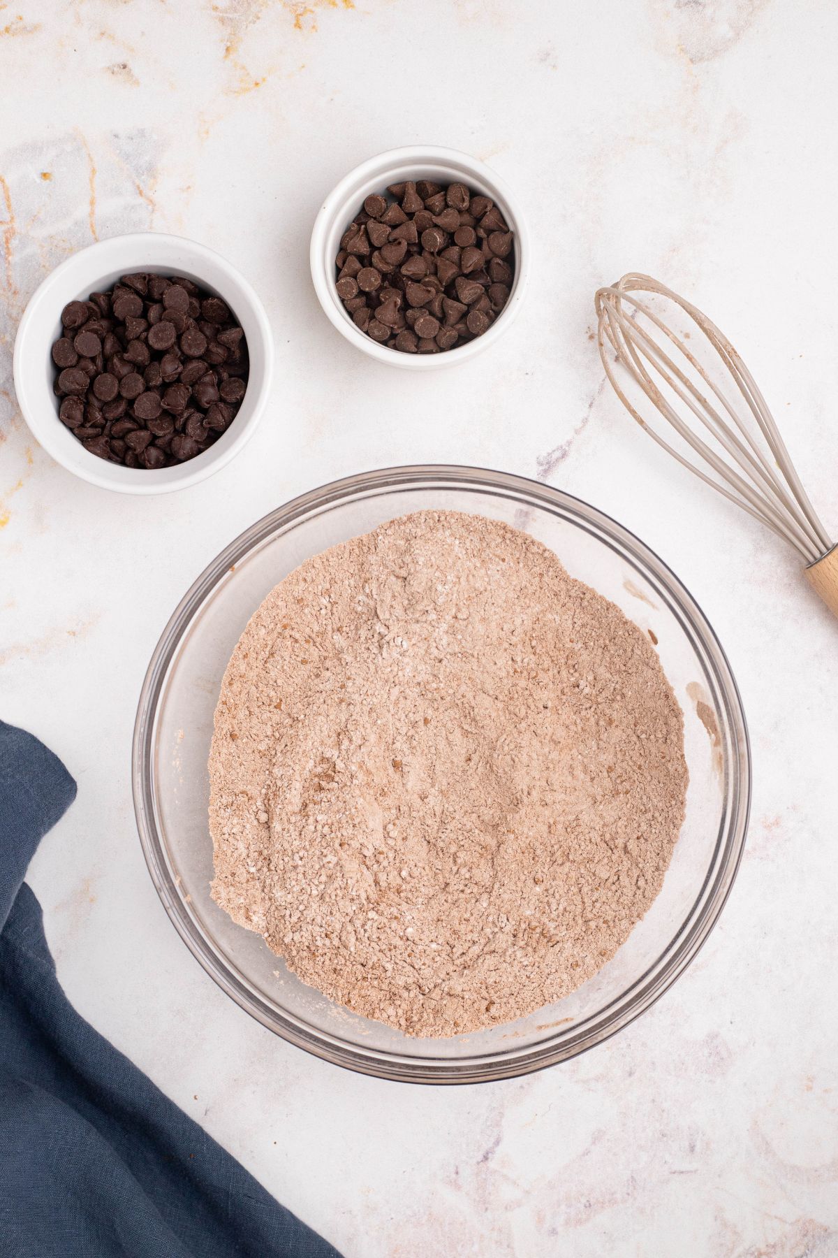 Flour and other dry ingredients being mixed together in clear glass bowl. 