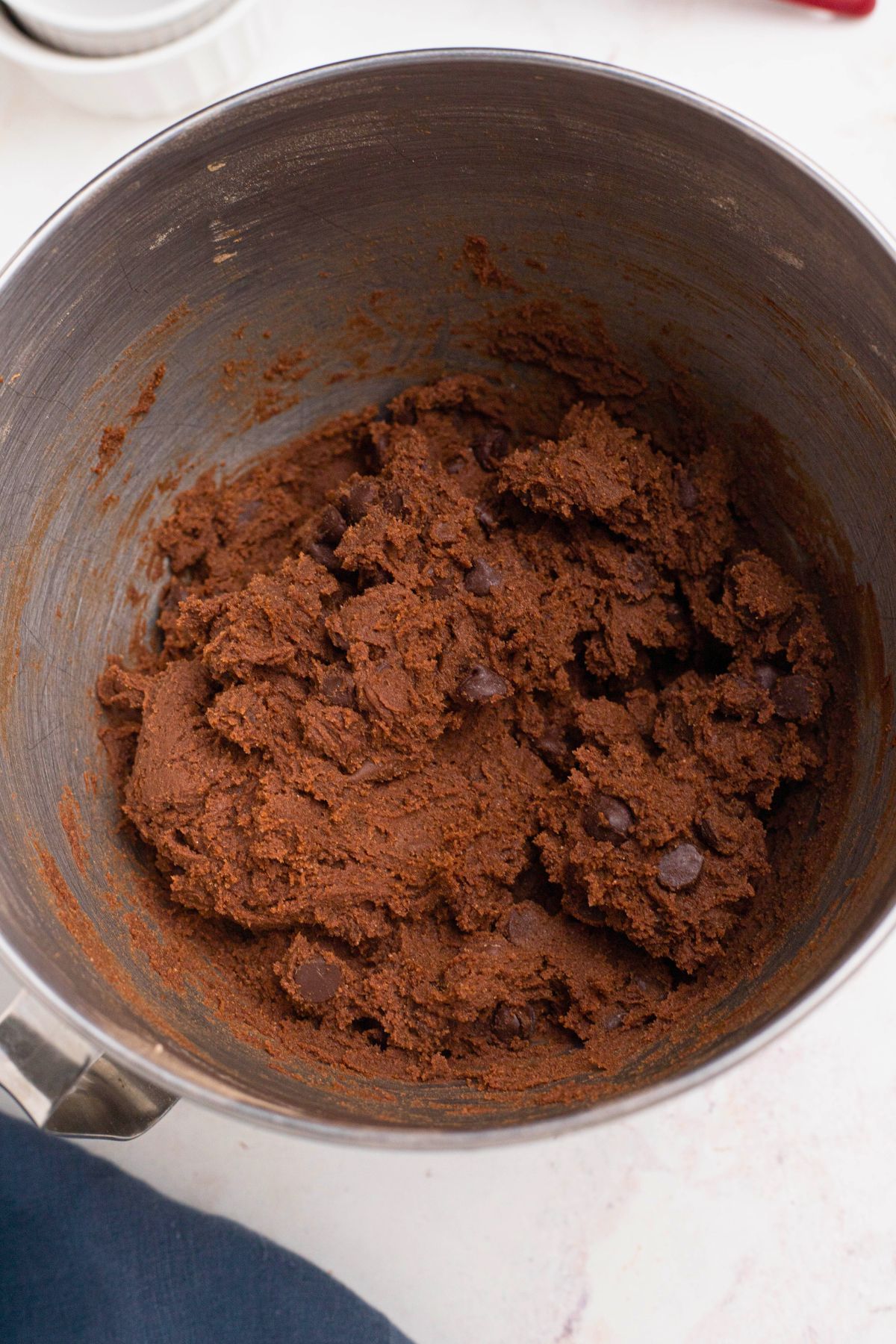 Chocolate dough with chocolate chips in a silver mixing bowl. 