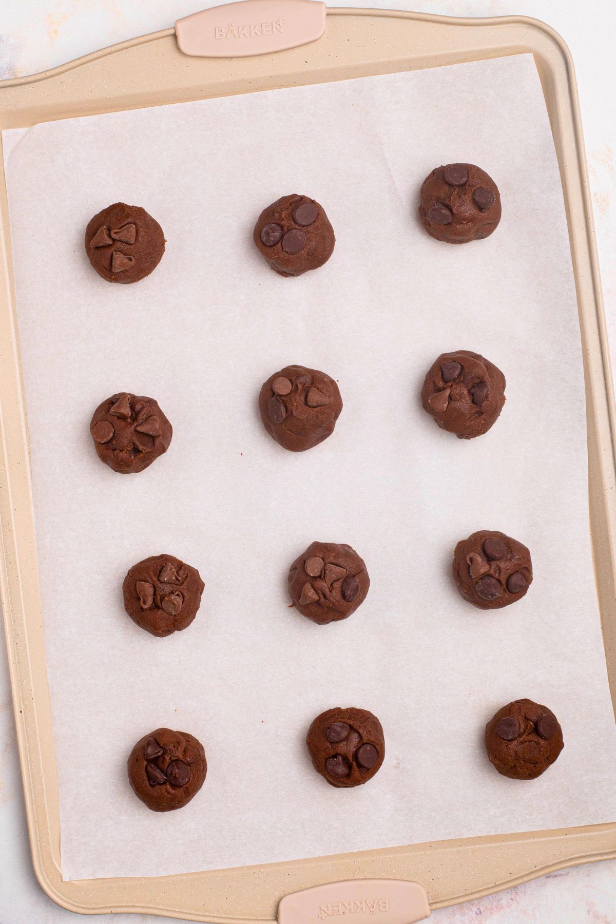 Cookie dough in balls, dropped onto baking sheet lined with parchment paper. 