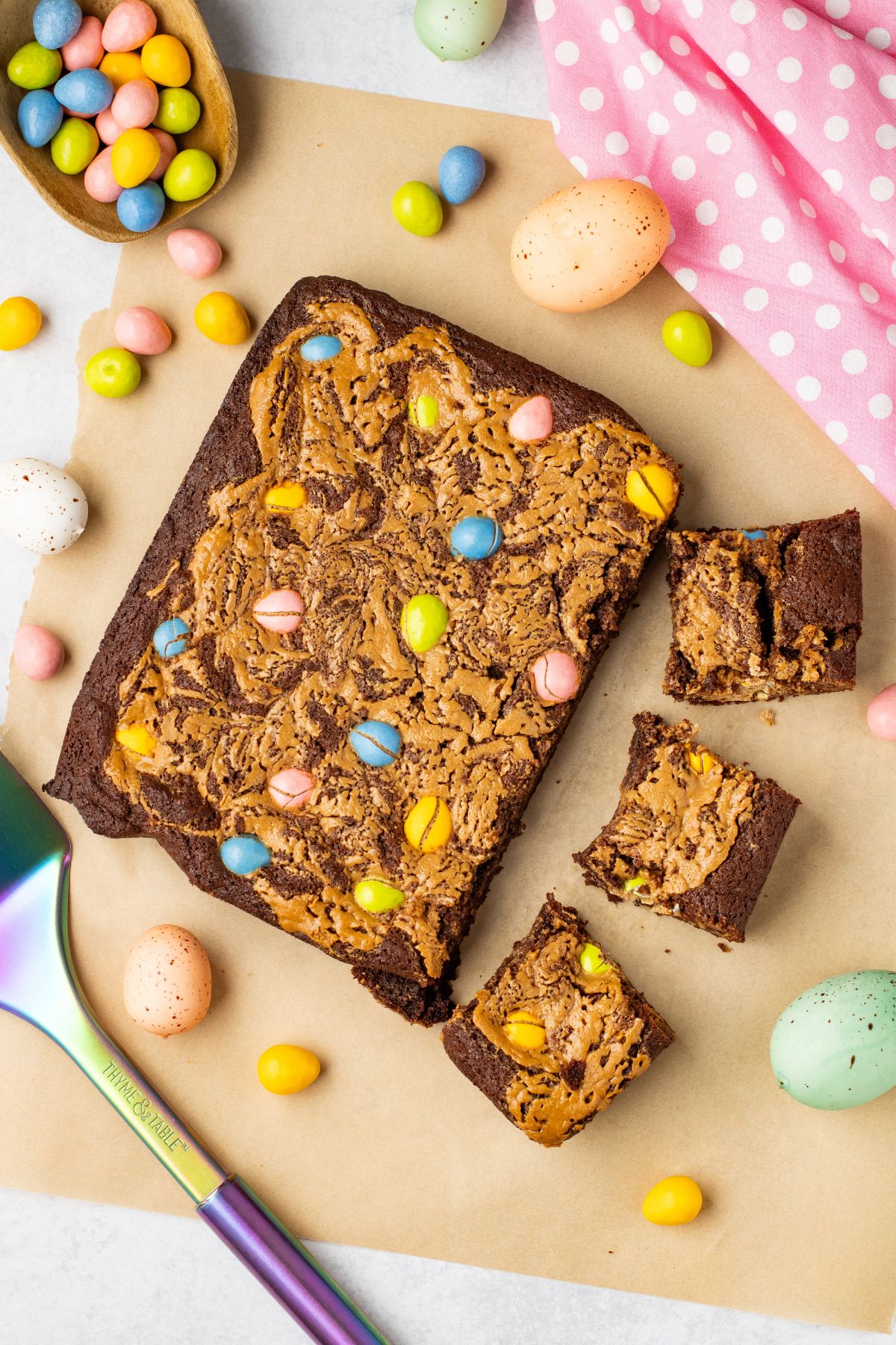 Easter brownies being cut into squares with candies on the table along with a pink linen. 