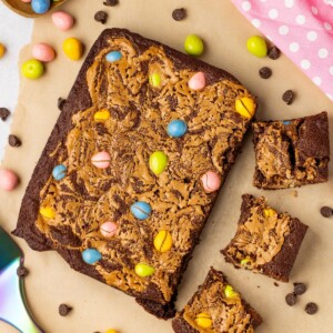 Easter brownies being cut into squares with candies on the table along with a pink linen.