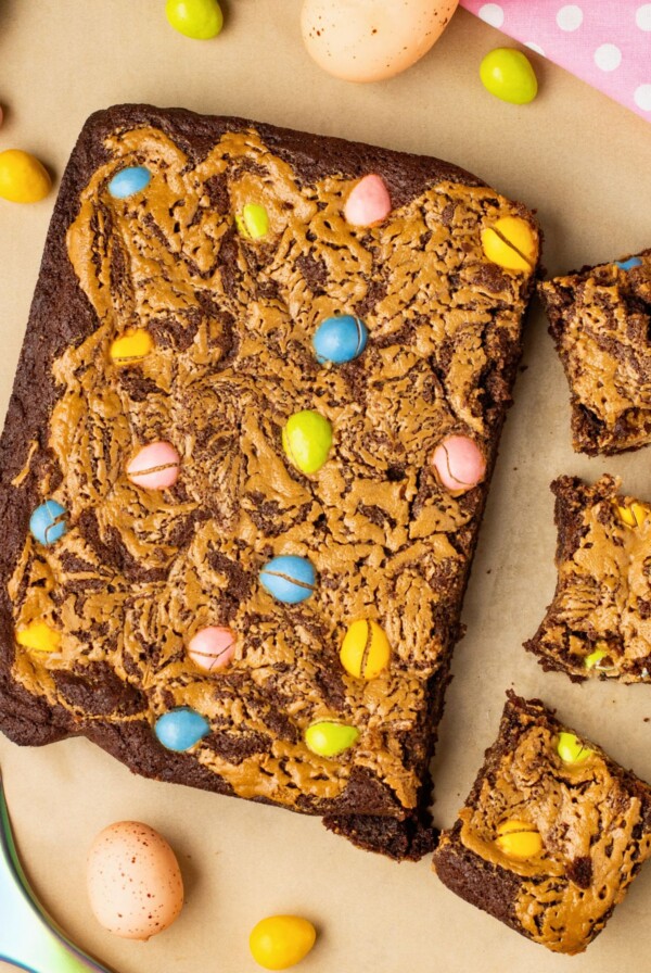 Easter brownies being cut into squares with candies on the table along with a pink linen.