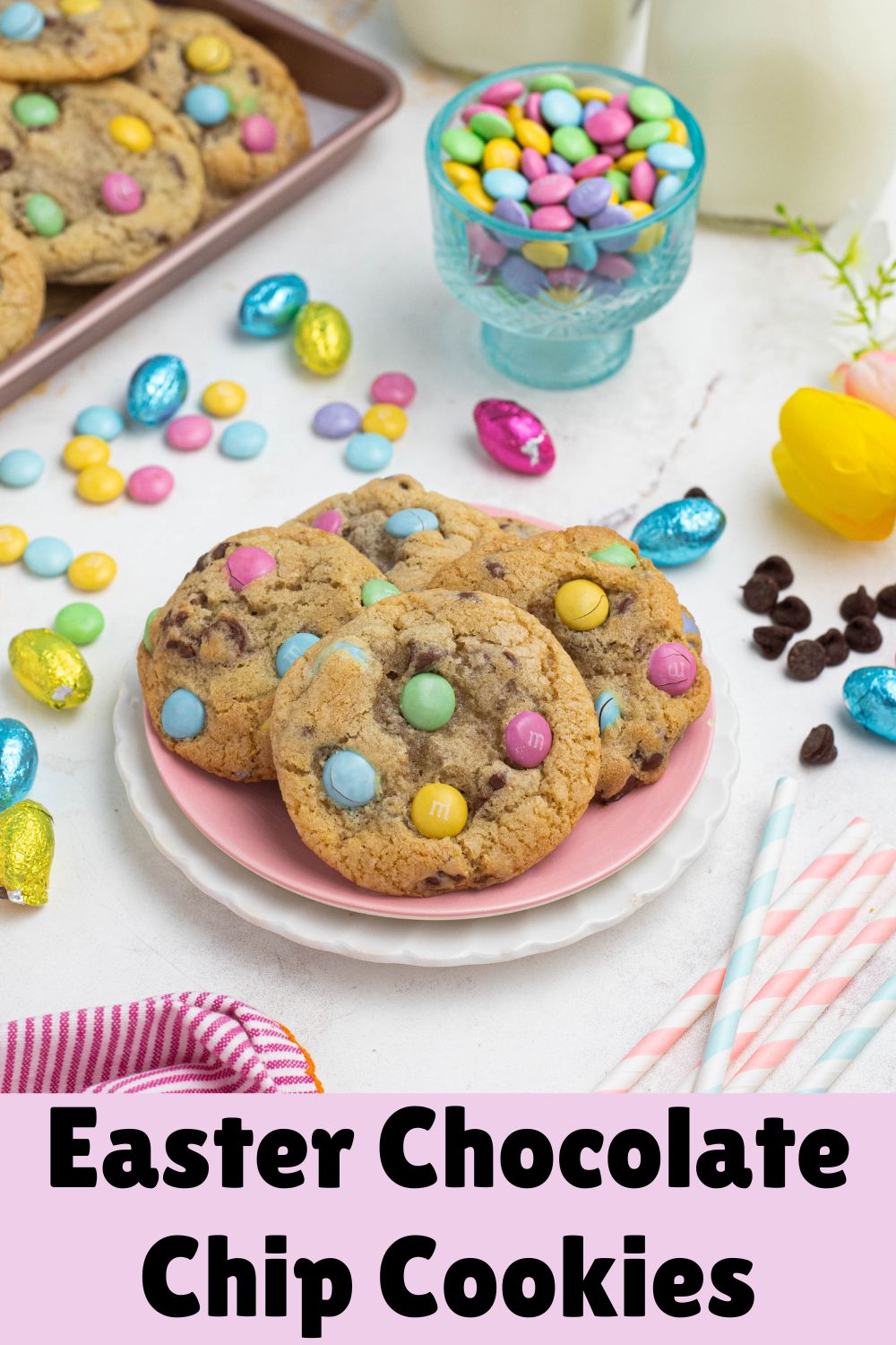 Golden chocolate chip cookies with pastel candies on plates, in front of candy dish and glasses of milk.