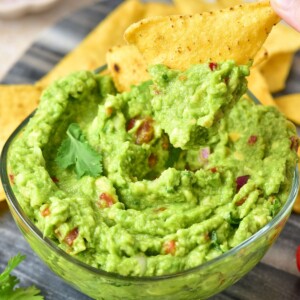 Creamy guacamole with chopped tomatoes and onions mixed in it, with tortilla chip being dipped into the bowl.