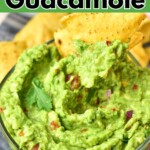 Creamy guacamole with chopped tomatoes and onions mixed in it, with tortilla chip being dipped into the bowl.