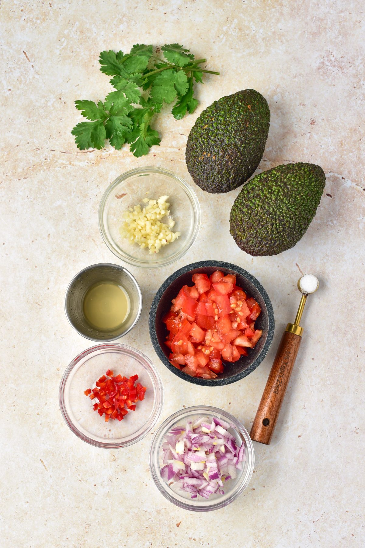 Ingredients needed for guacamole in small bowls on a marble table. 