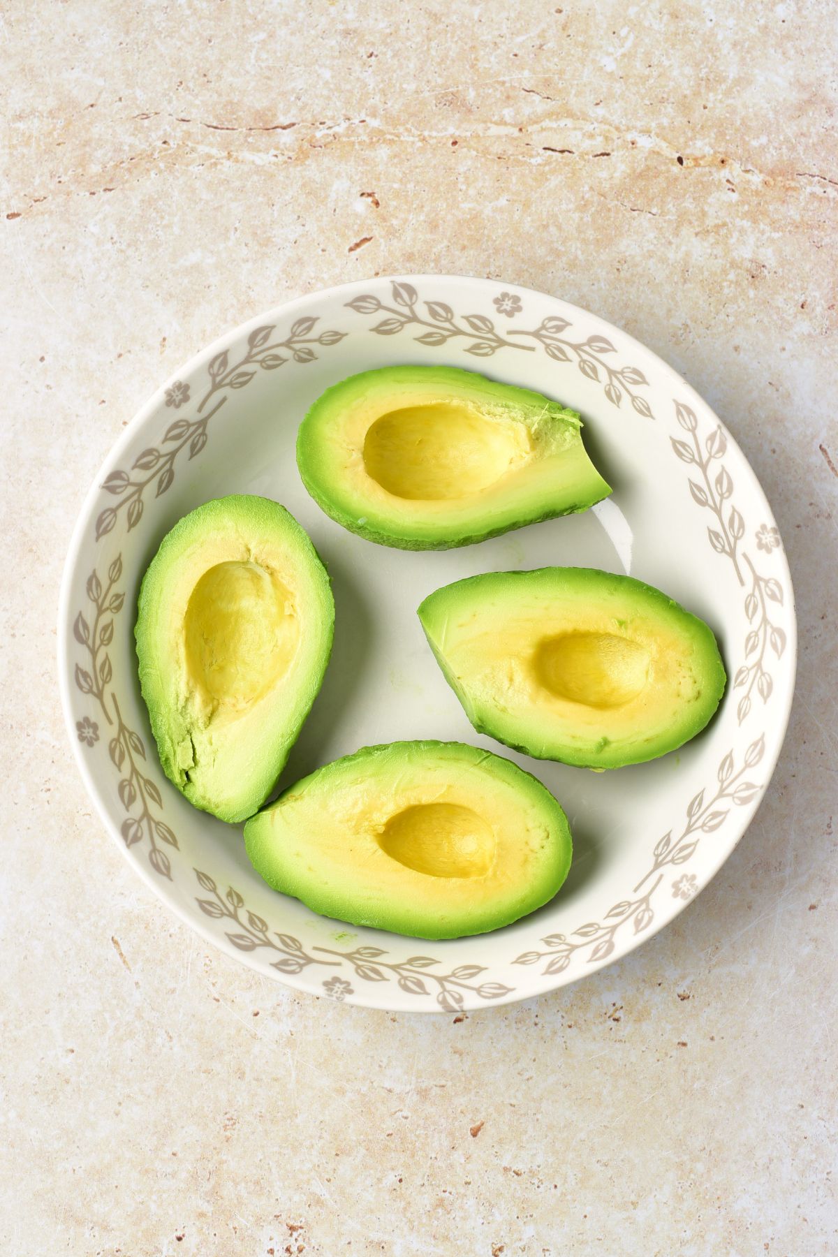 Avocados cut in half with pits removed in a bowl. 