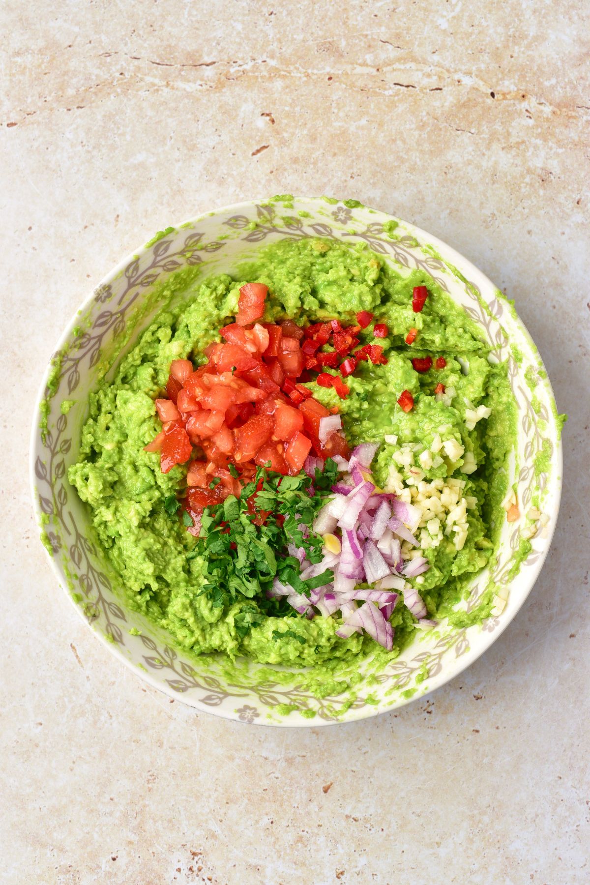 Chopped tomato, onions, and other ingredients on top of mashed avocados before being mixed in to make guacamole. 