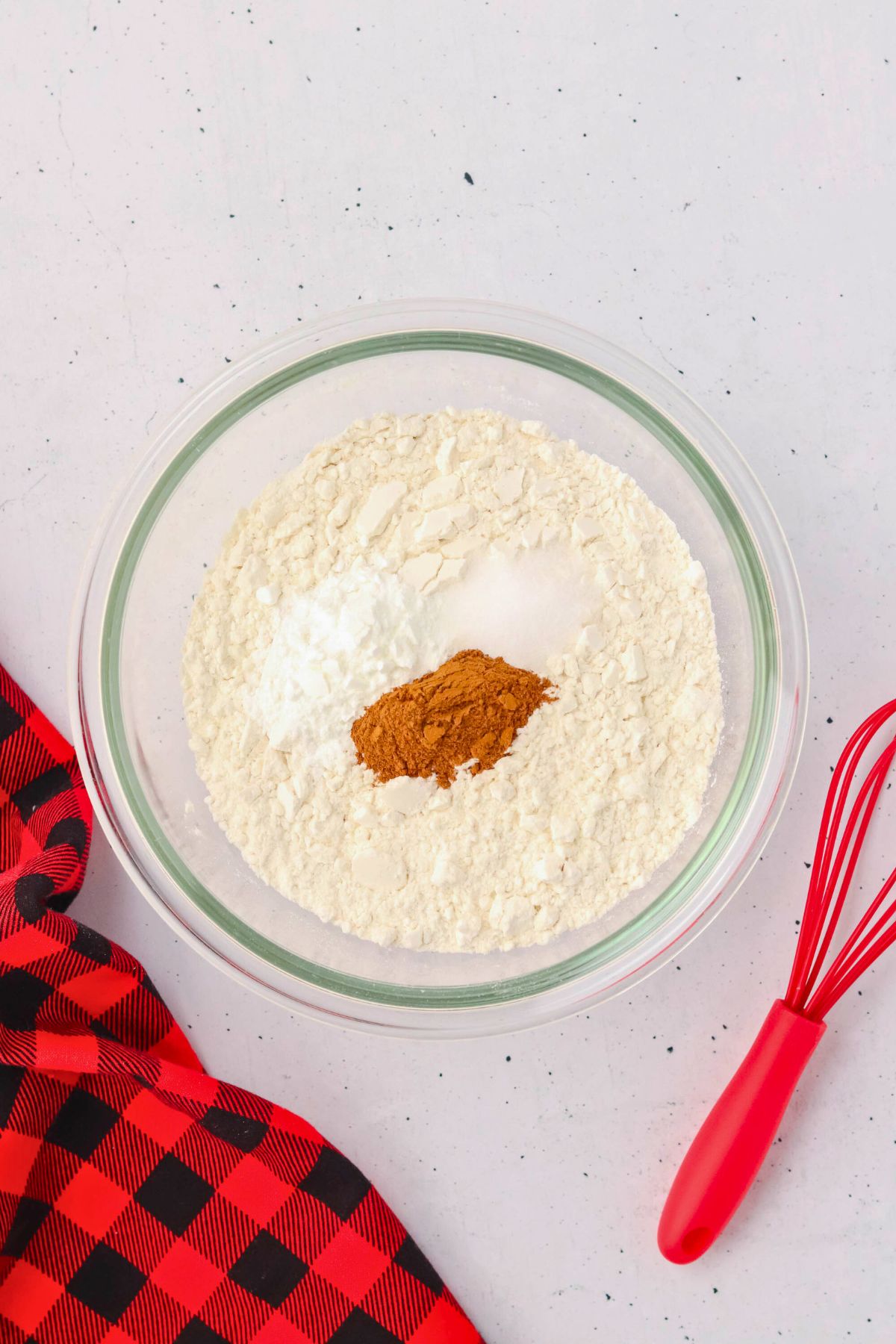 Flour and other dry ingredients being mixed in a glass bowl. 