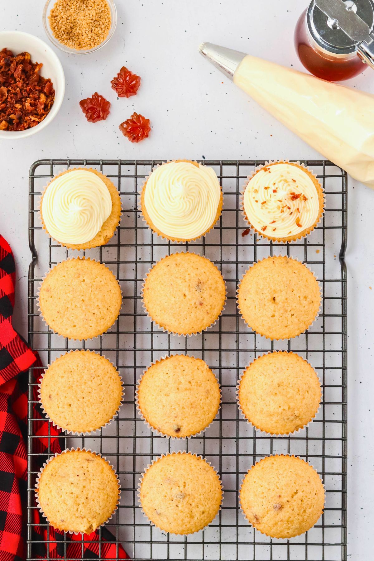 Baked cupcakes being frosted with maple bacon cream cheese frosting. 