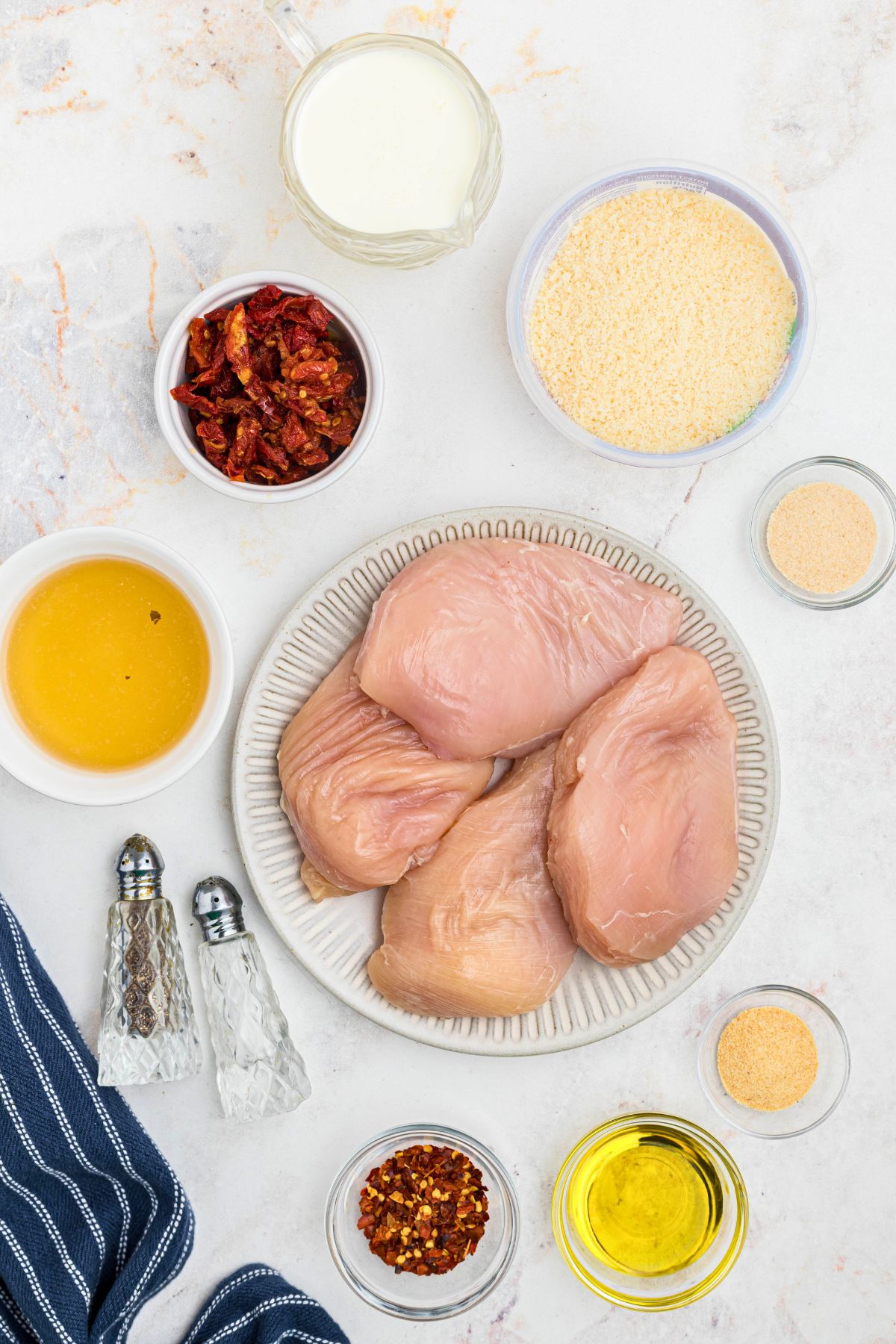 Ingredients needed to make Marry me Chicken measured into small bowls, on a marble table. 
