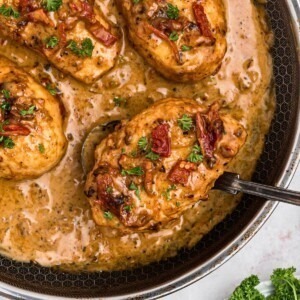 Creamy chicken in a large skillet with a spoon lifting a piece out of skillet.