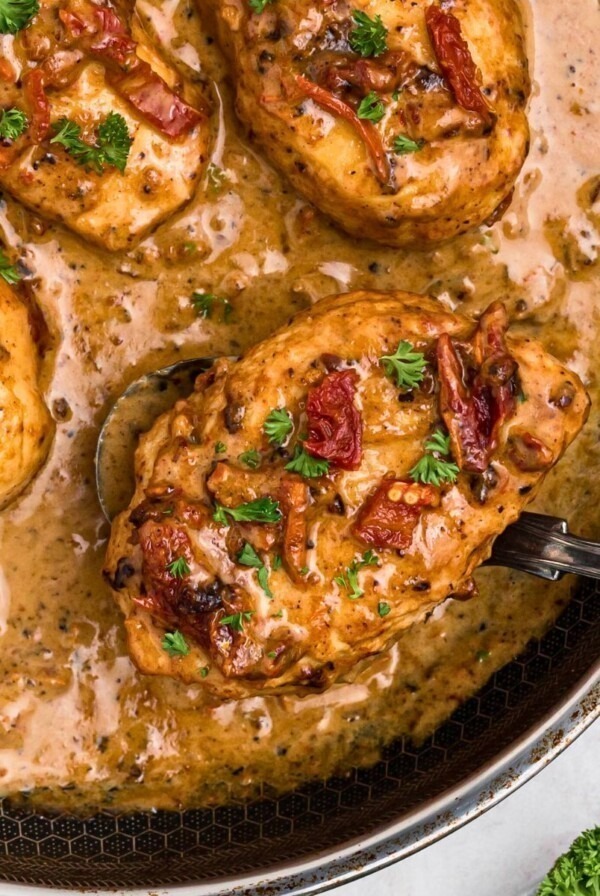Creamy chicken in a large skillet with a spoon lifting a piece out of skillet.
