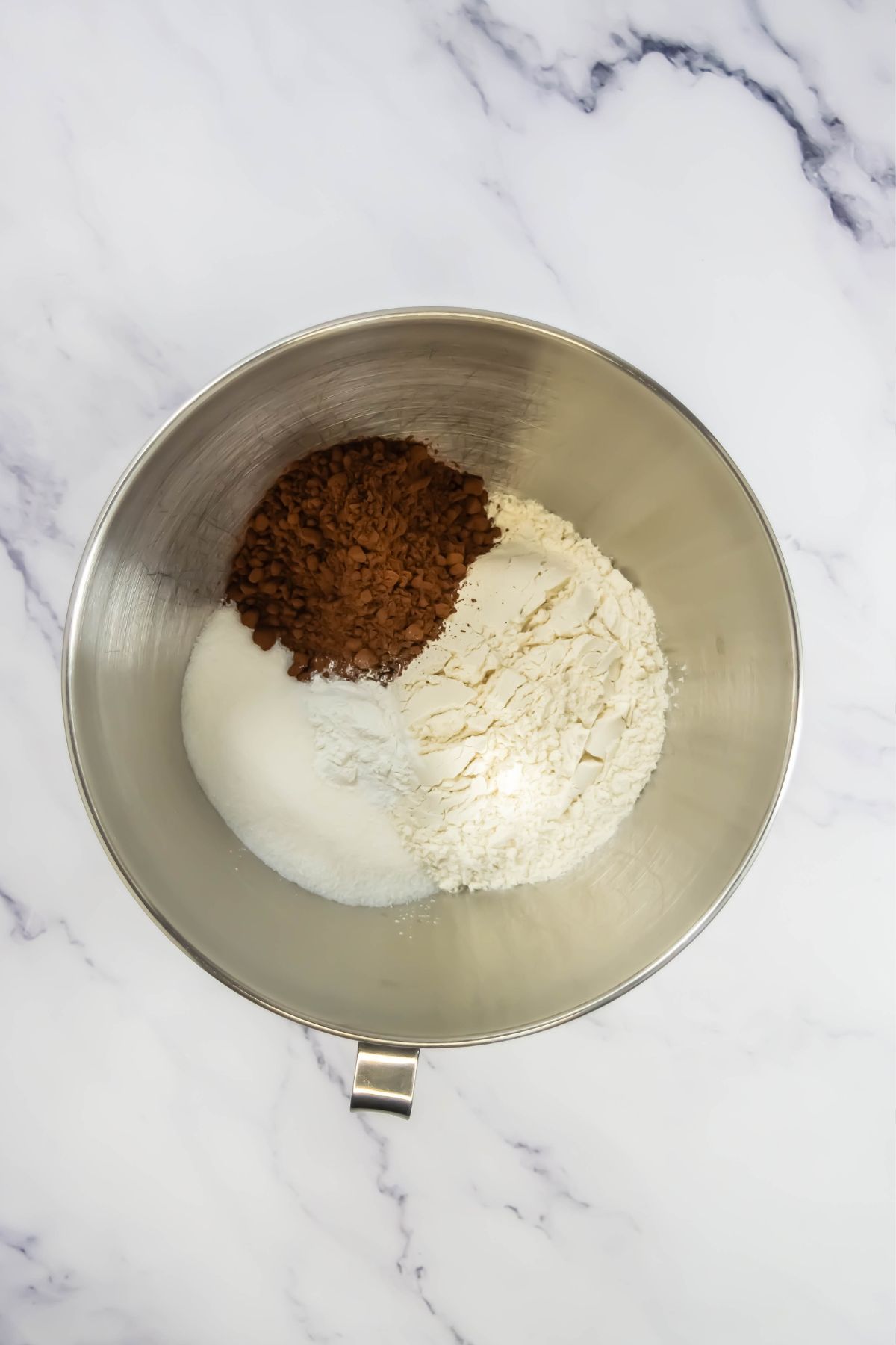 Dry ingredients like flour and cocoa powder in a silver mixing bowl. 