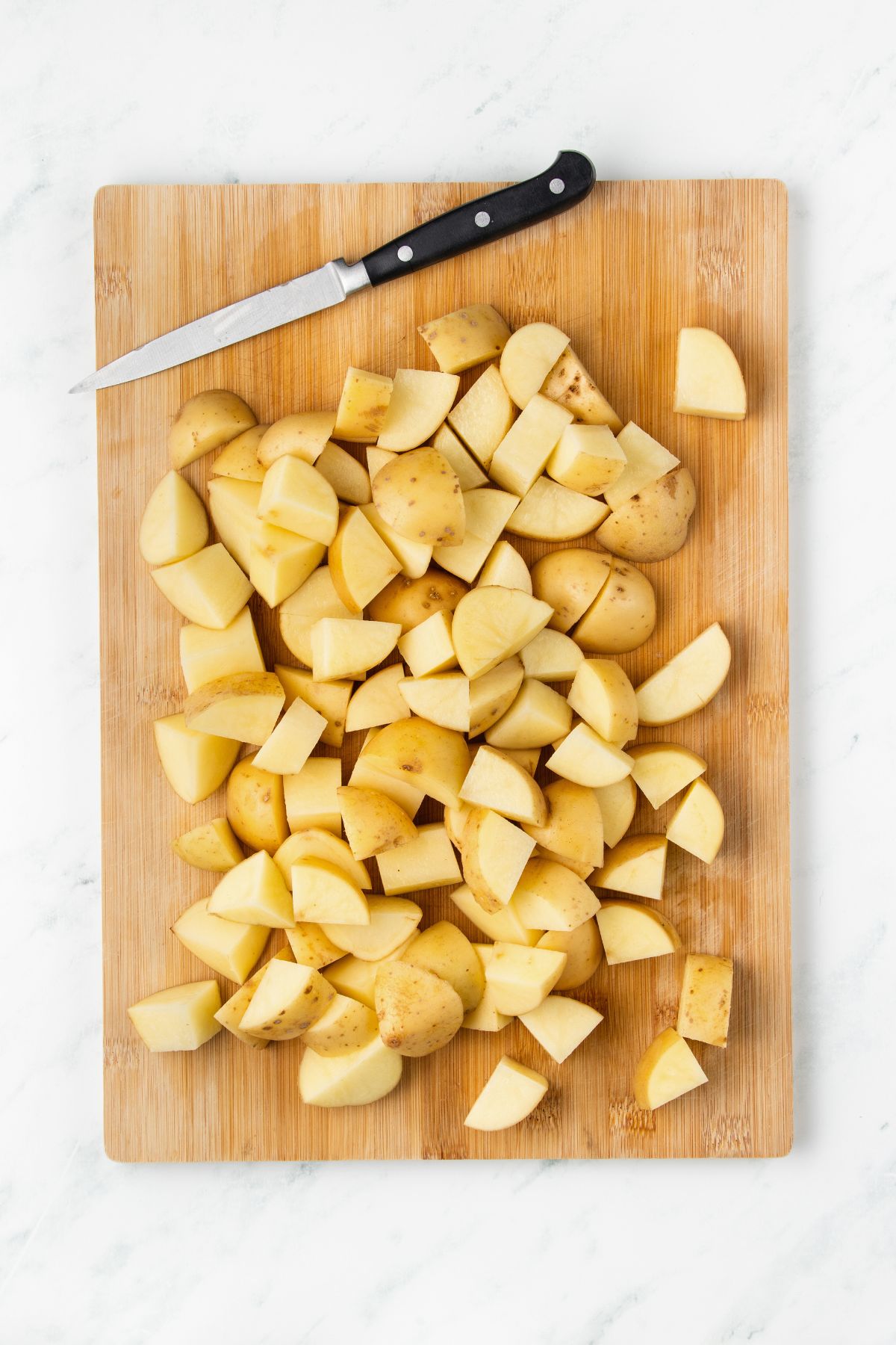 Potatoes cut into small pieces on a wooden cutting board. 