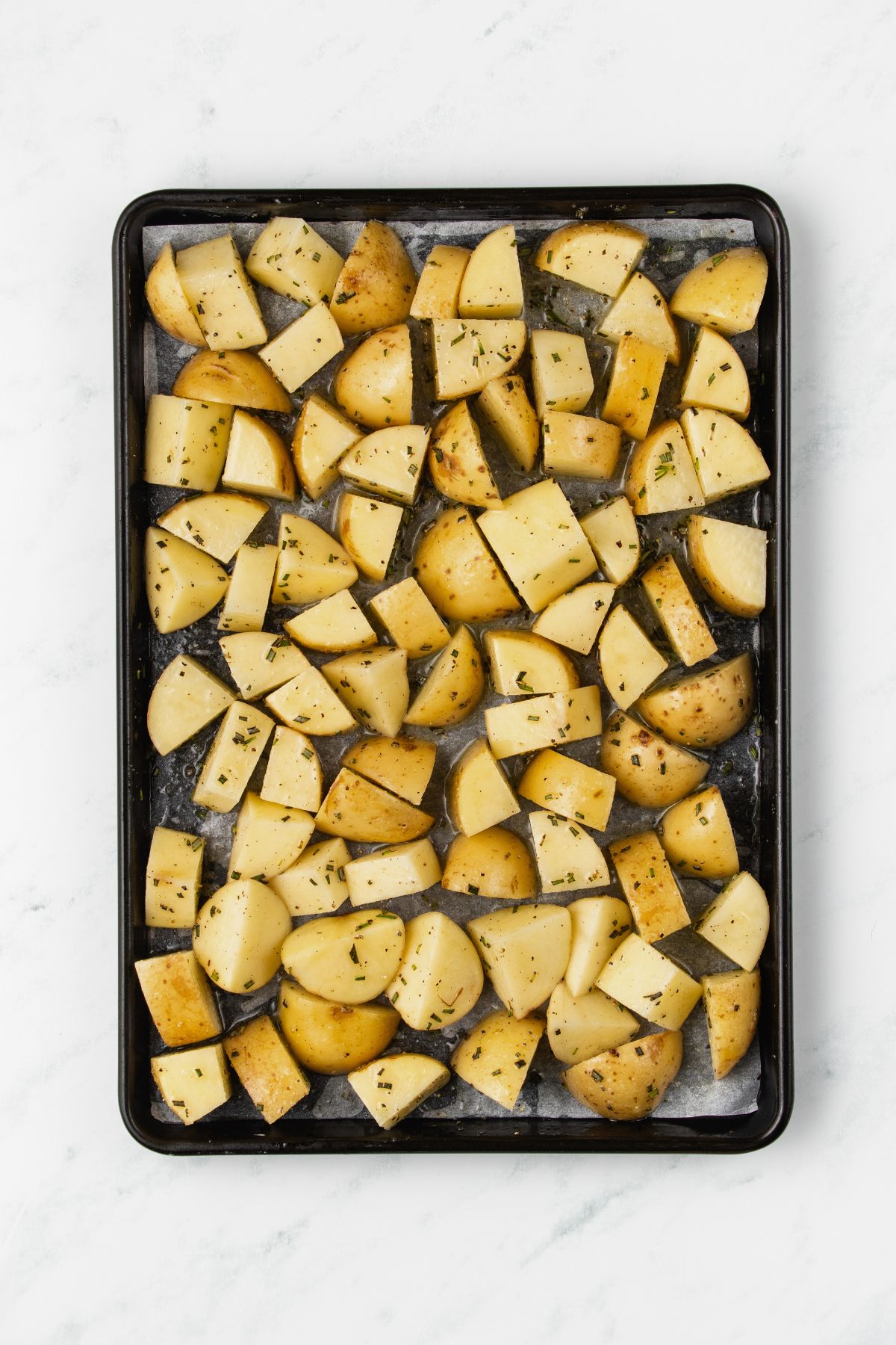Potatoes cut into pieces, then seasoned, before being baked. 