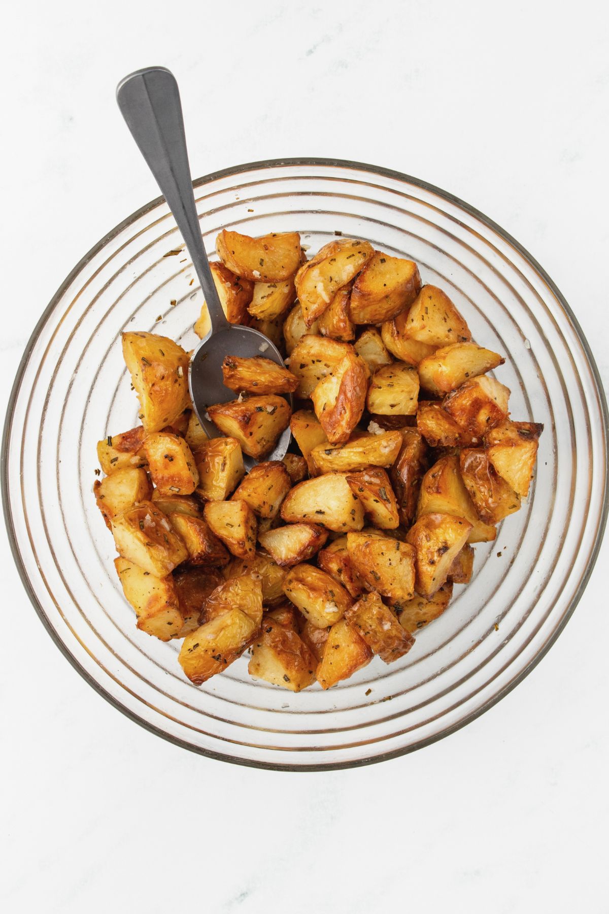 Pieces of potatoes being tossed with lemon juice and garlic in a large bowl. 