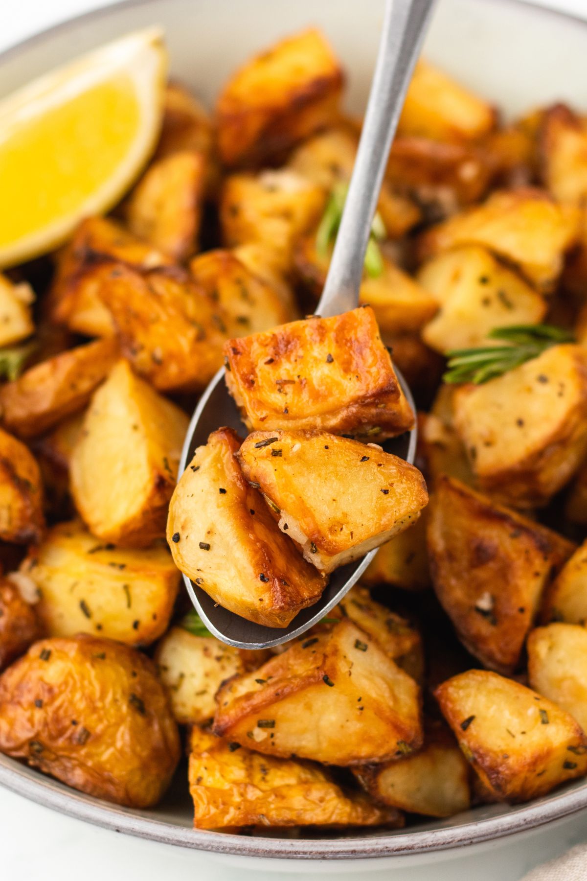 Easy garlic roast potatoes in a white bowl with a spoonful lifting a serving out.