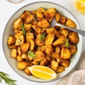 Sliced potatoes in a white bowl with a spoonful lifting a serving out.