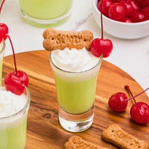 Green liquid in a shot glass, topped with graham cracker snack and bright red cherry.