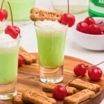 Green drink in a shot glass topped with cool whip and a red cherry.