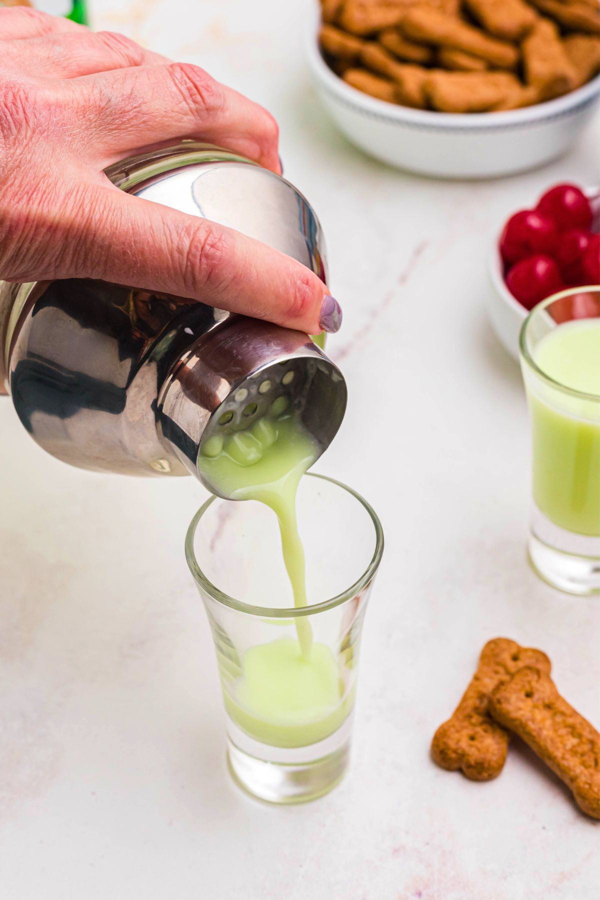 Green liquid cocktail ingredients being strained into shot glass. 