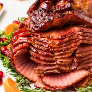 Spiral ham cut into slices on a white platter with bread rolls on the table.