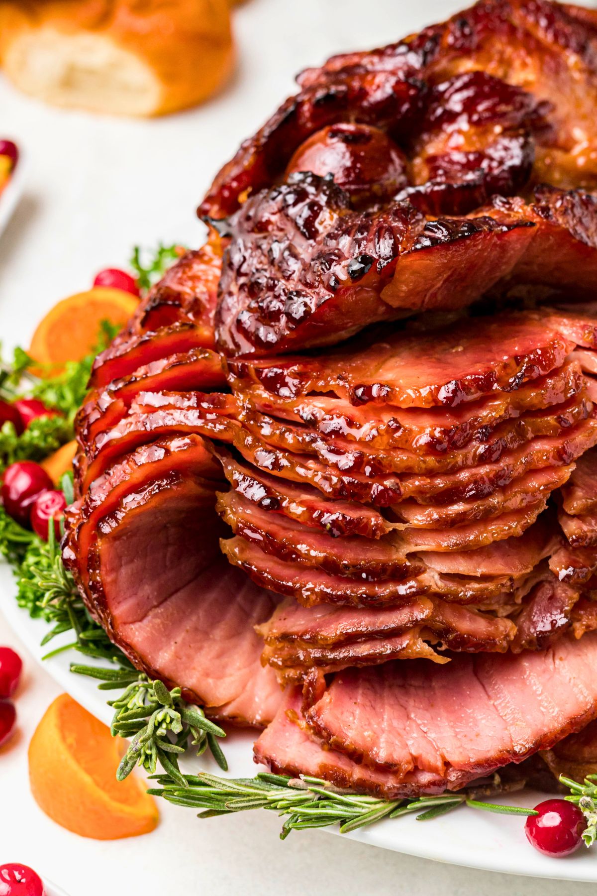 Spiral ham cut into slices on a white platter with bread rolls on the table. 