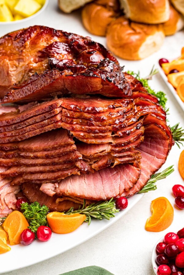 Golden juicy sliced ham on a white platter with cranberry and orange slices as a garnish.