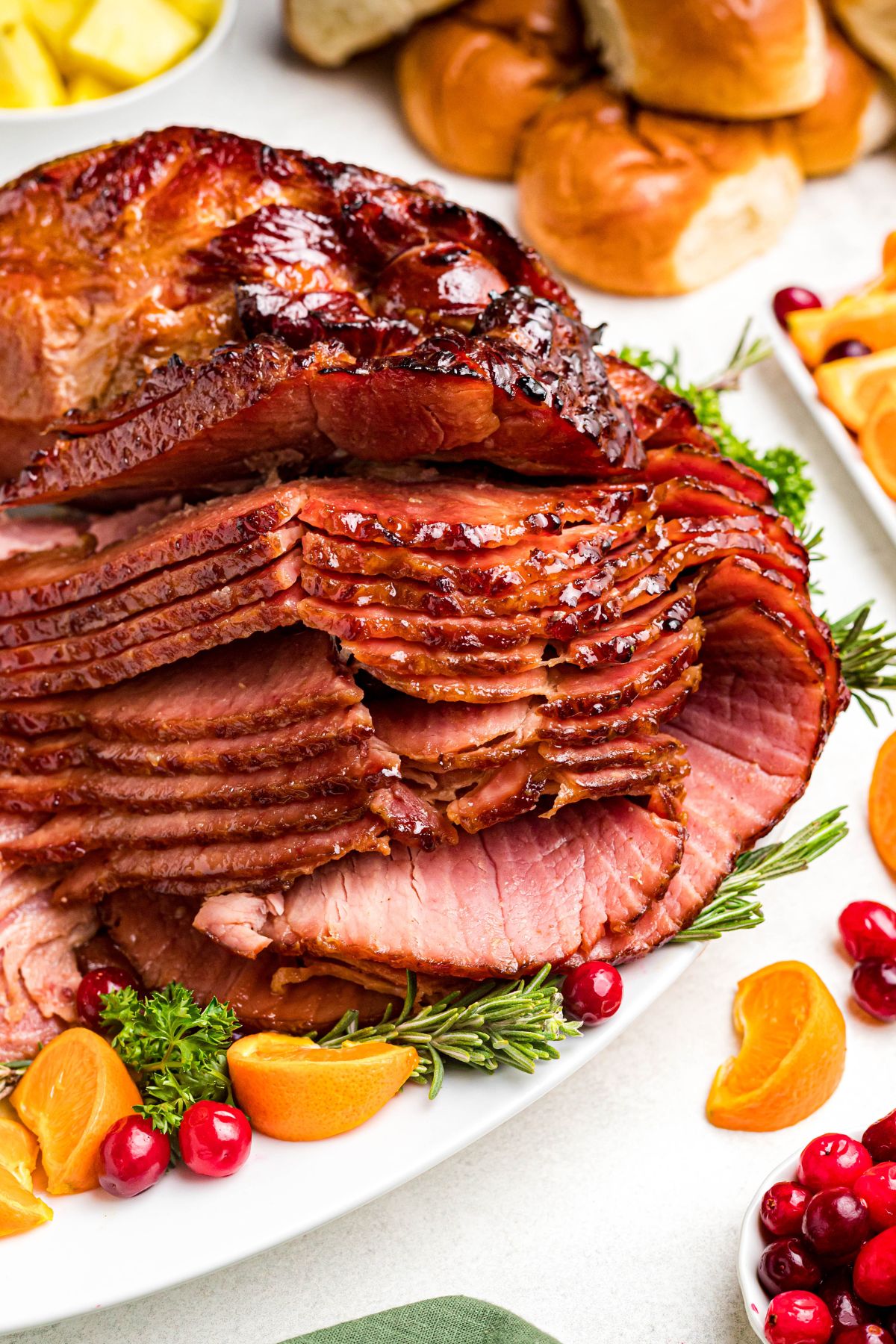 Golden juicy sliced ham on a white platter with cranberry and orange slices as a garnish. 