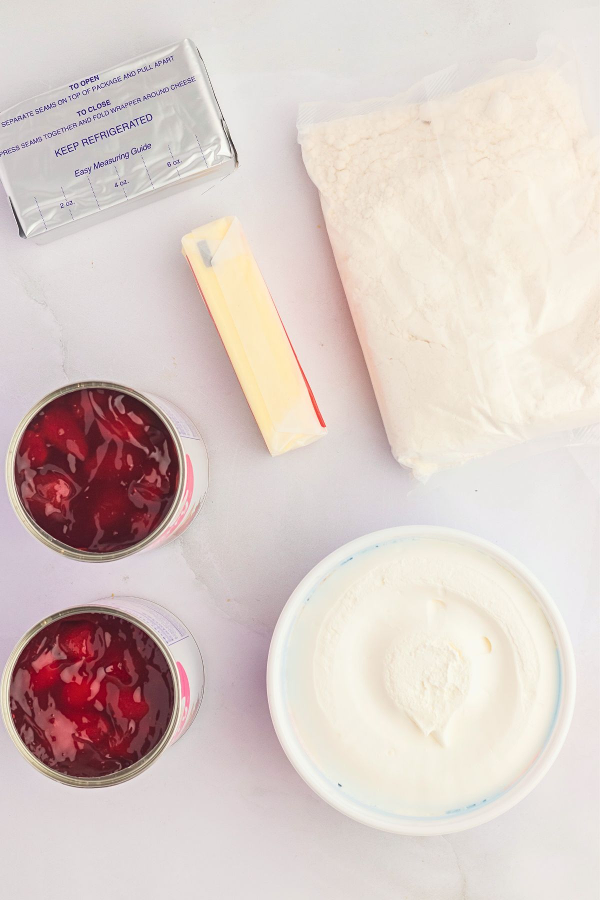 Ingredients needed to make strawberry dump cake on a white marble table. 