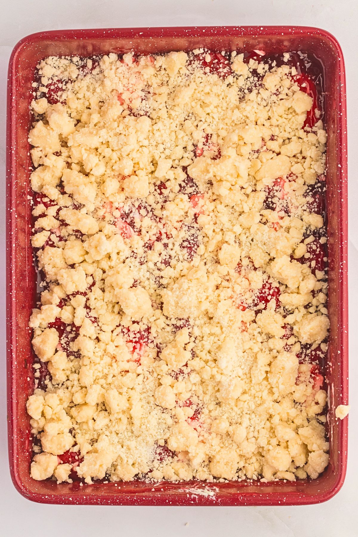 Uncooked cake mix mixed with butter dolloped on top a strawberry pie filling. 