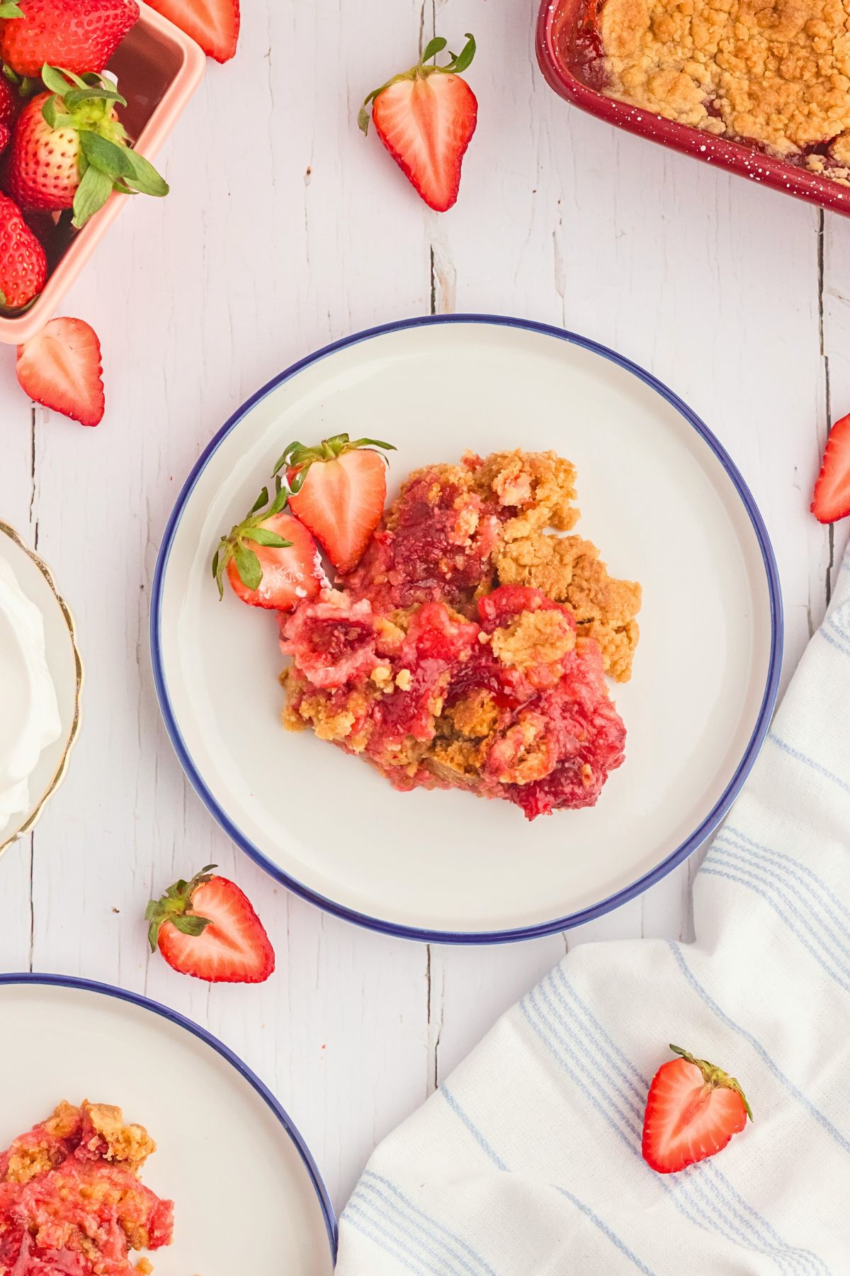 Strawberry dump cake on a white plate with strawberry slices scattered around the plate. 