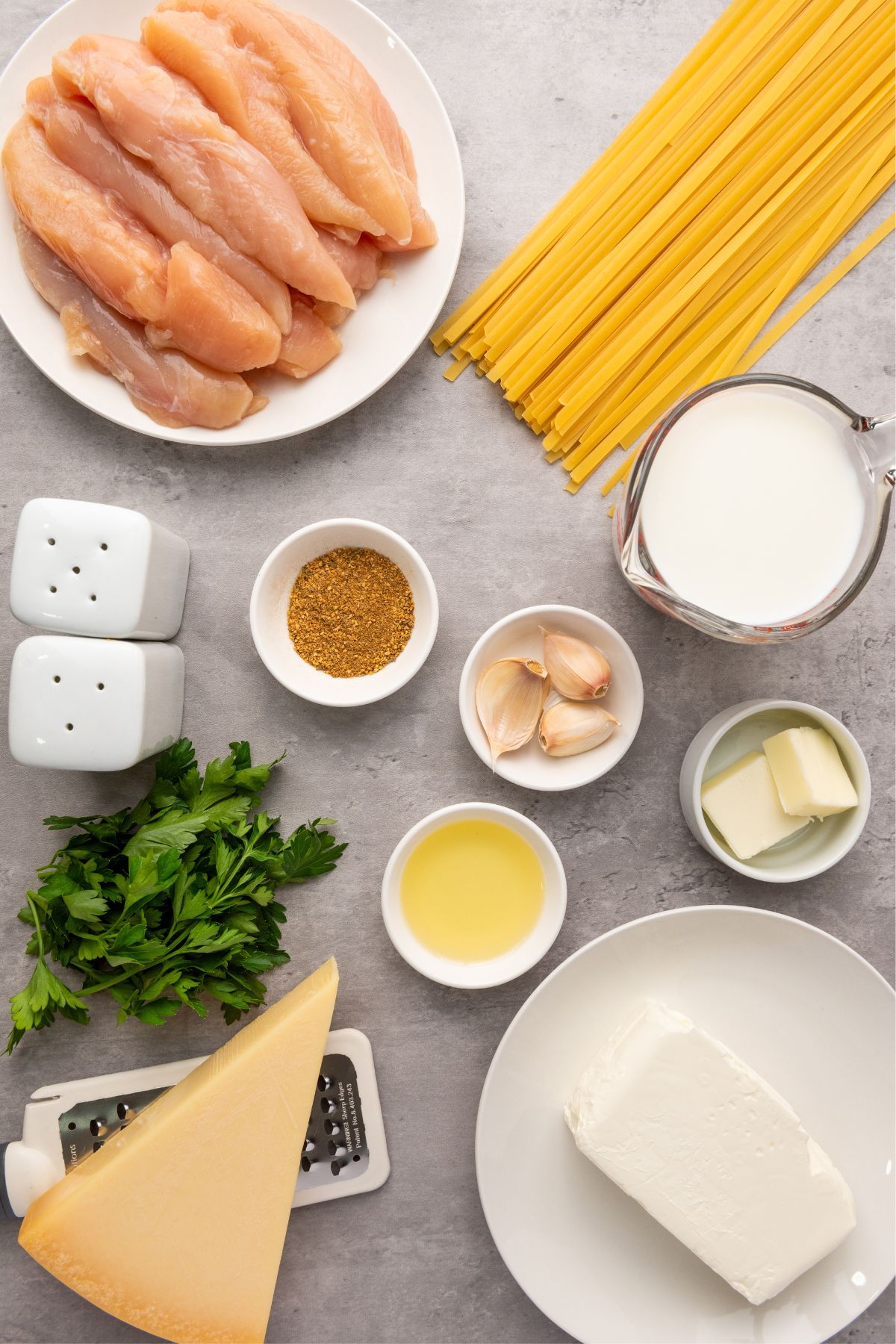 Ingredients needed to make chicken alfredo measured into small jars on a marble table. 