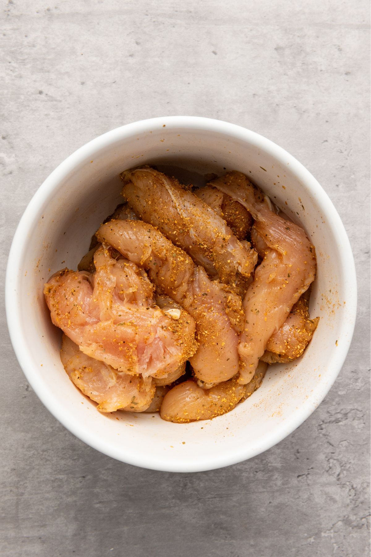 Uncooked chicken, seasoned, in a white bowl. 