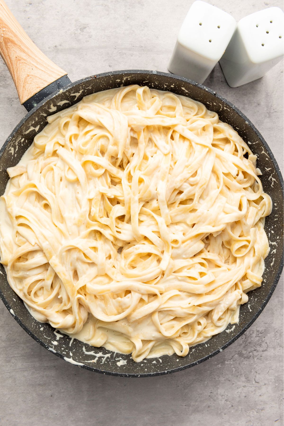 Alfredo sauce tossed with cooked pasta in a skillet. 