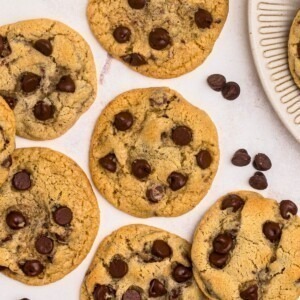 Golden brown chocolate chip cookies on a marble table with chips scattered around them.