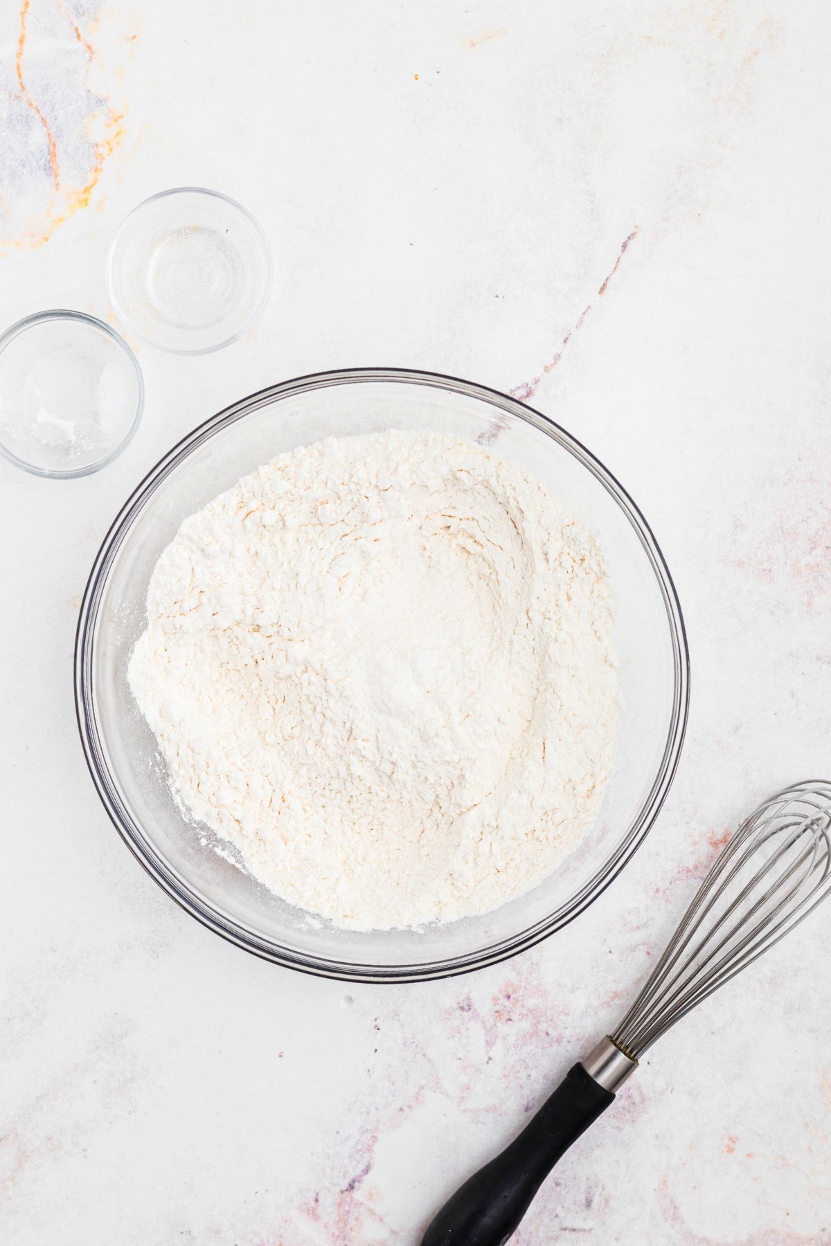Flour and other ingredients mixed in a clear glass bowl. 