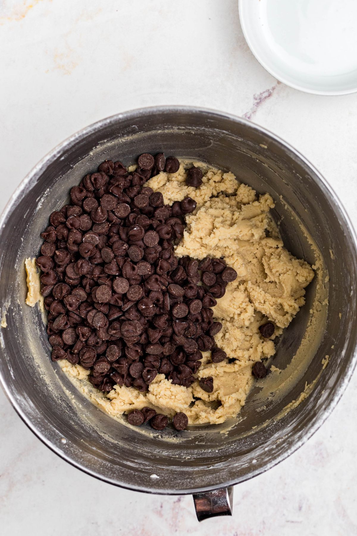 Soft dough in a mixing bowl with chocolate chips being added. 