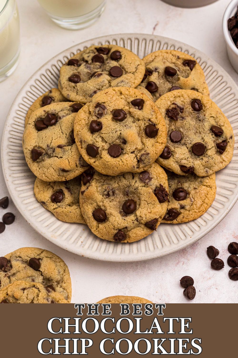 Chocolate chip cookies stacked on a white plate with chips and other cookies around them.
