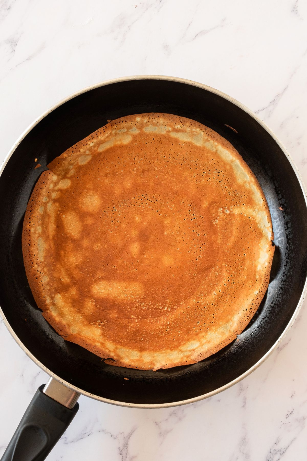 Very thin crepes being made in a black skillet, cooked until golden brown. 