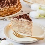 Golden light and fluffy slice of cake make from layers of thin crepes, served on a white plate.