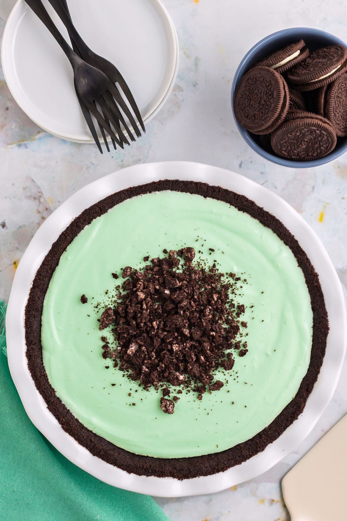 Grasshopper pie in a white pie dish with oreos on the table. 
